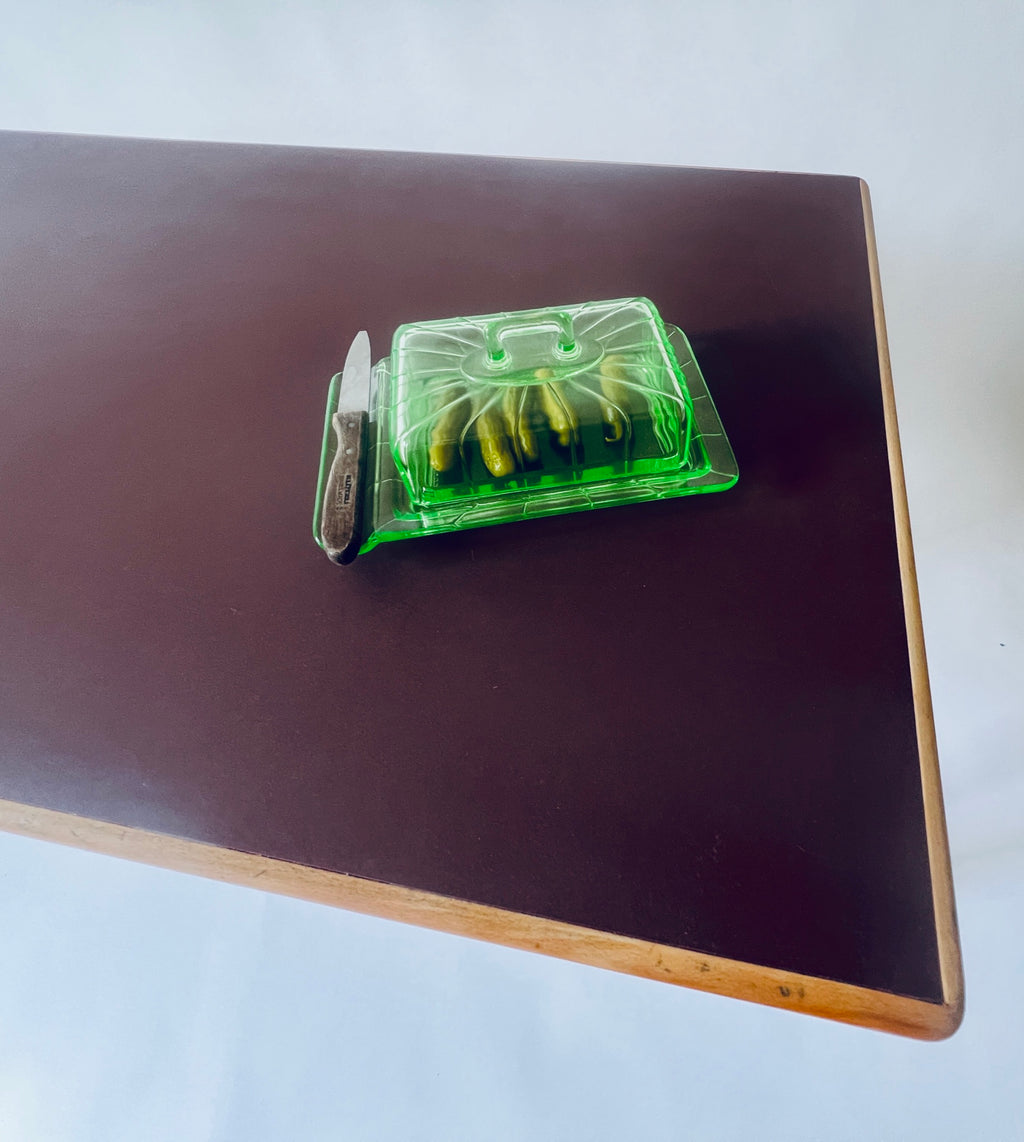 Ansicht der burgunderroten Forbo-Linoleumoberfläche mit Holzumrandung und einer grünen Glasschale mit Deckel.
