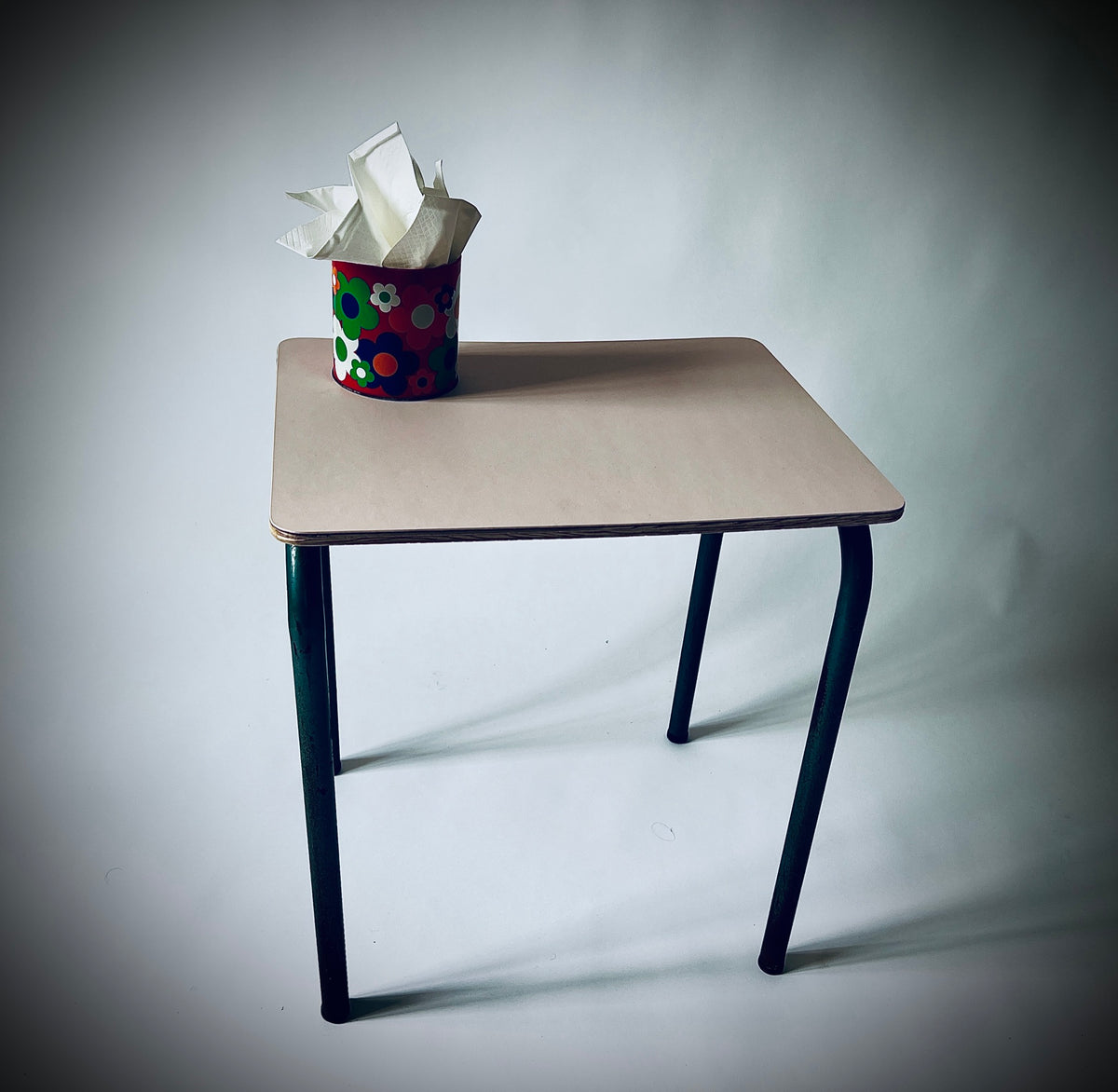 Beistelltisch Châtenois/Keschteholz mit hellrosa Linoleumplatte und dunkelgrünem Metallgestell, darauf eine bunte Dose mit Papiertüchern.