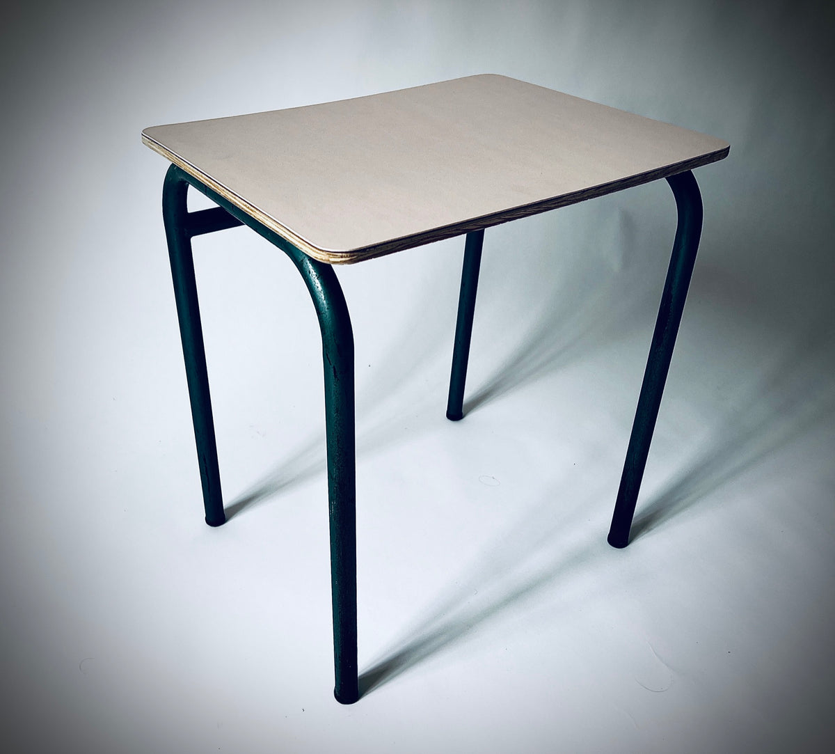 Schrägansicht des Beistelltischs mit hellrosa Forbo-Linoleum, sichtbarer Holzkante und gebogenen dunkelgrünen Metallbeinen.

