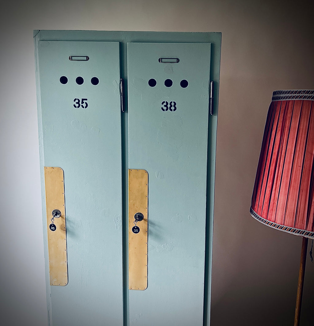 Blaugrüner Garderobenschrank mit zwei Türen, den Nummern 35 und 38, runden Lüftungslöchern und langen gelblichen Schutzplatten.