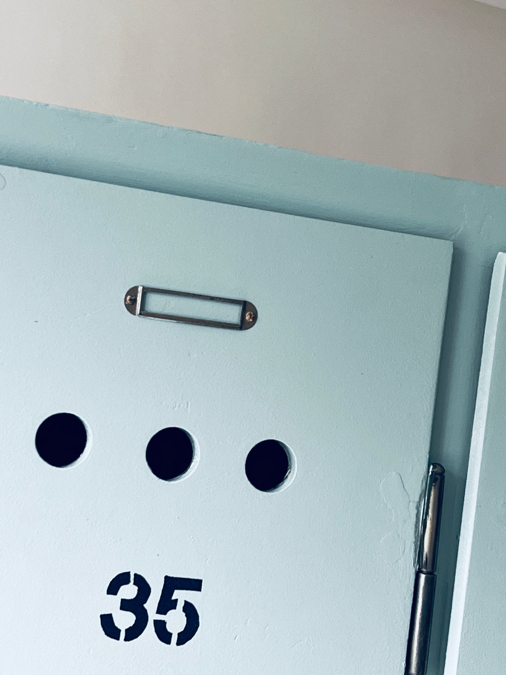 Oberer Teil der Tür 35 mit metallischem Beschriftungshalter, drei Lüftungslöchern und aufgemalter Nummer.
