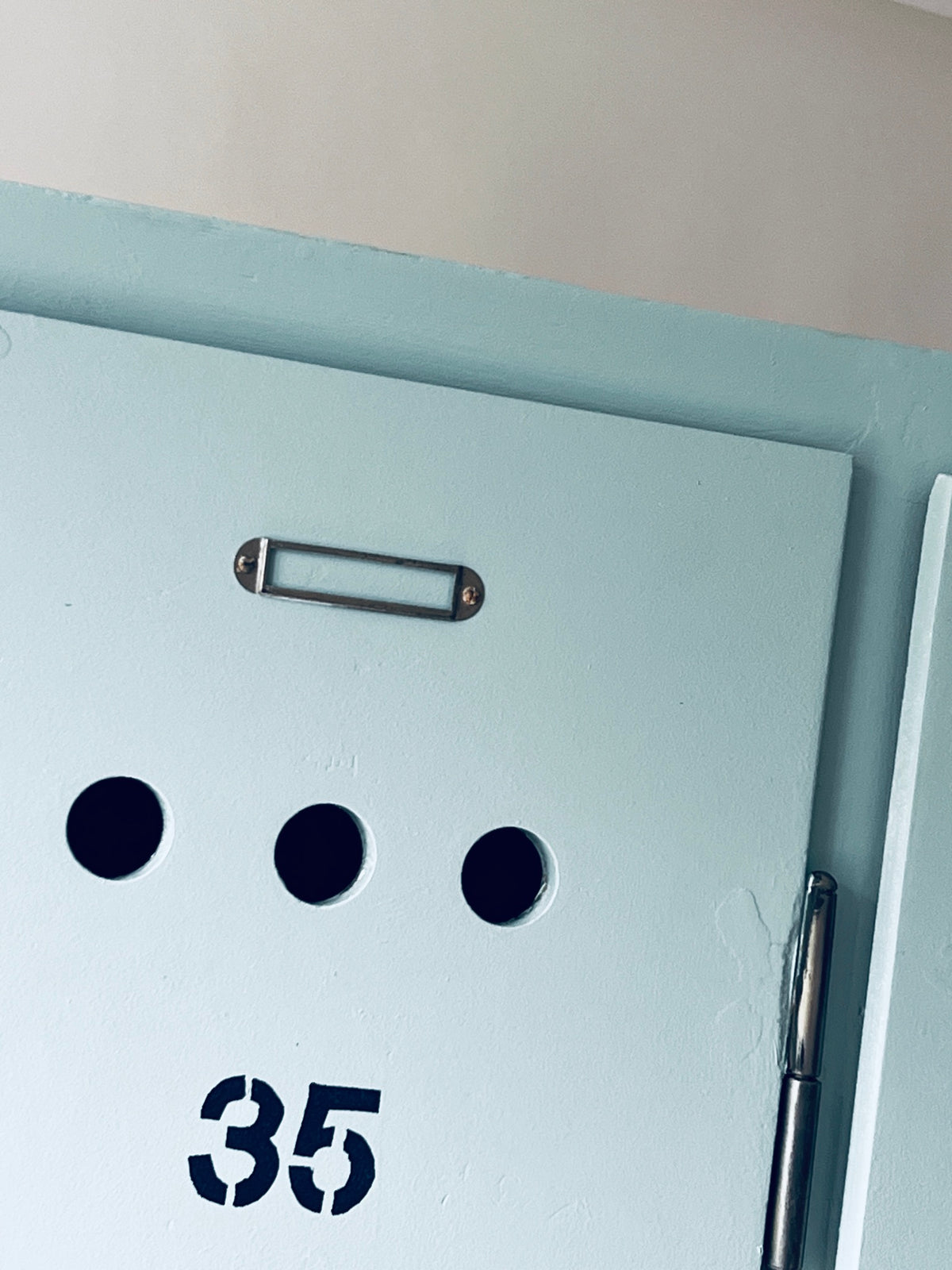 Oberer Teil der Tür 35 mit metallischem Beschriftungshalter, drei Lüftungslöchern und aufgemalter Nummer.
