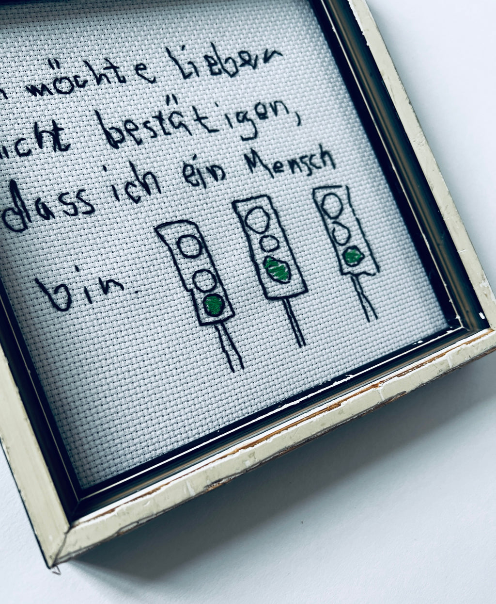 Detailansicht der drei gestickten grünen Ampeln, eines Teils des Schriftzugs und des weiss-schwarzen Rahmens mit Gebrauchsspuren.